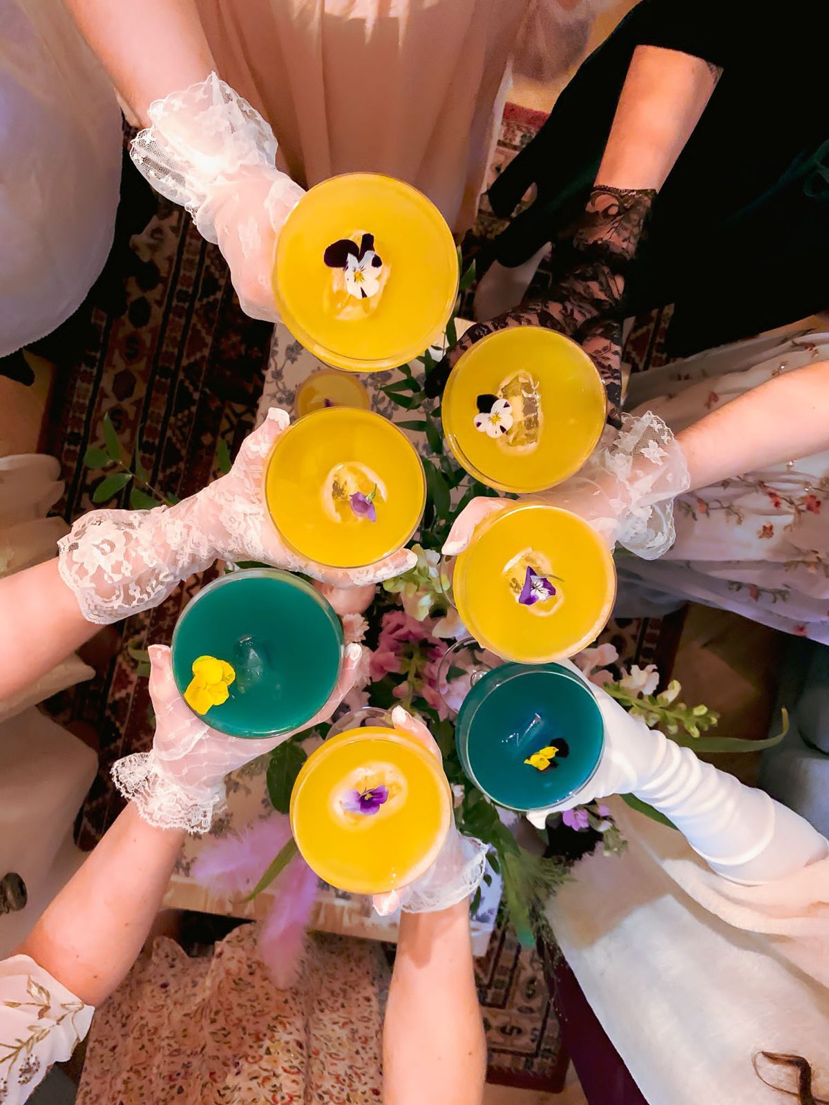 Invitées d'une murder party en gants de dentelle qui trinquent avec des cocktails fleuris